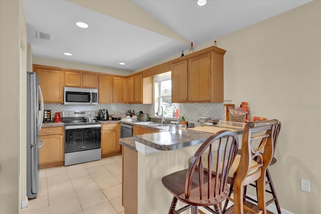 kitchen with a peninsula, a sink, visible vents, appliances with stainless steel finishes, and decorative backsplash