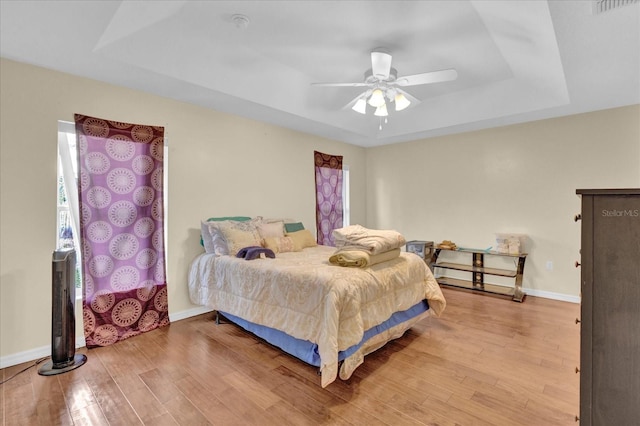 bedroom with visible vents, baseboards, a raised ceiling, ceiling fan, and wood finished floors