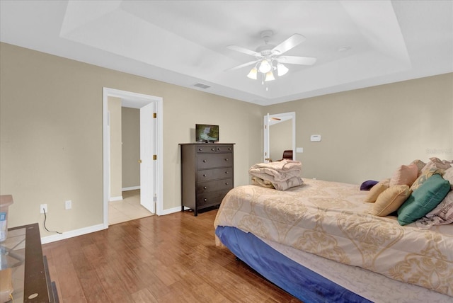 bedroom with baseboards, visible vents, ceiling fan, wood finished floors, and a tray ceiling