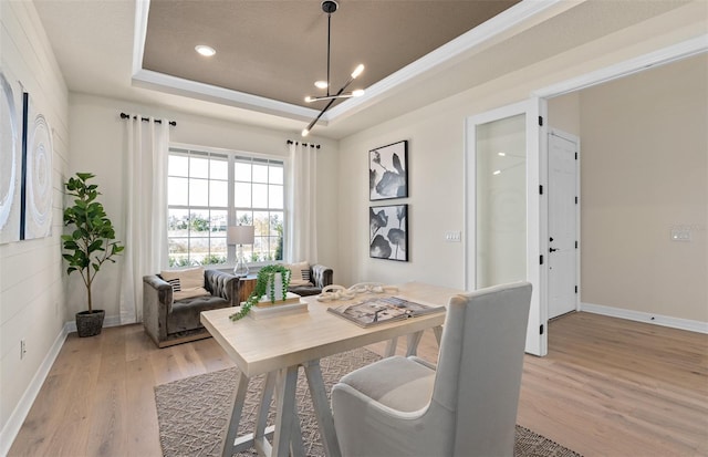 dining space featuring an inviting chandelier, light wood-style flooring, a tray ceiling, and baseboards