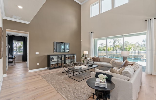 living area with baseboards, a towering ceiling, light wood-style flooring, and crown molding