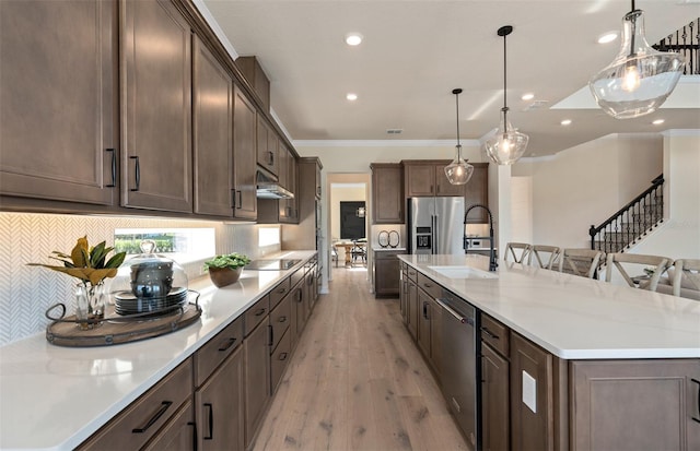 kitchen with stainless steel appliances, a sink, light wood-type flooring, a large island with sink, and crown molding