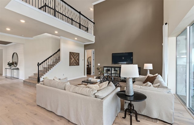 living room with ornamental molding, a high ceiling, light wood finished floors, and stairs