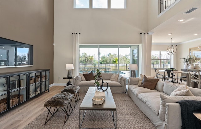 living area featuring a notable chandelier, visible vents, a high ceiling, wood finished floors, and baseboards