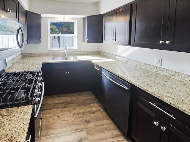 kitchen with stainless steel appliances, light wood-type flooring, a sink, and light stone counters