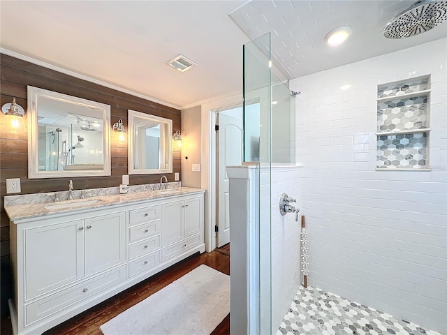 bathroom with double vanity, tiled shower, a sink, and visible vents