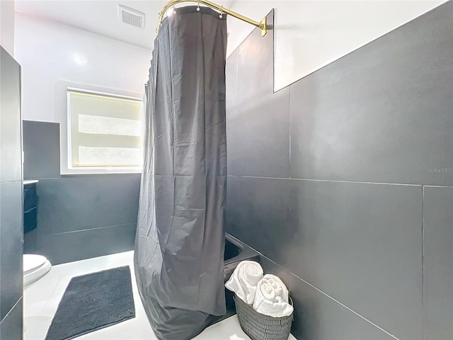 bathroom with toilet, visible vents, a shower with shower curtain, and tile walls