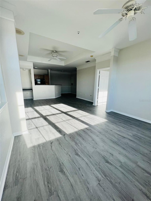 unfurnished living room featuring a tray ceiling, ceiling fan, baseboards, and wood finished floors