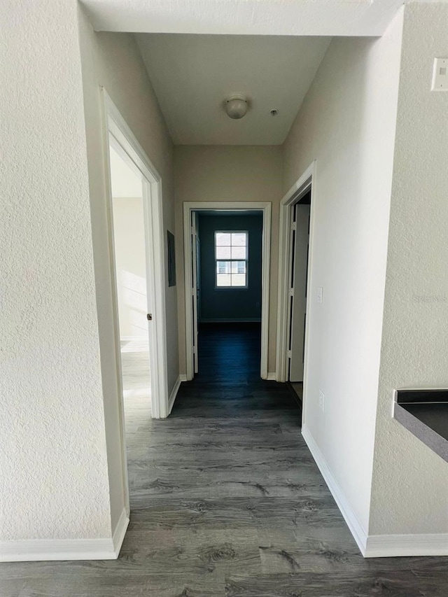 hall featuring dark wood-style flooring, a textured wall, and baseboards