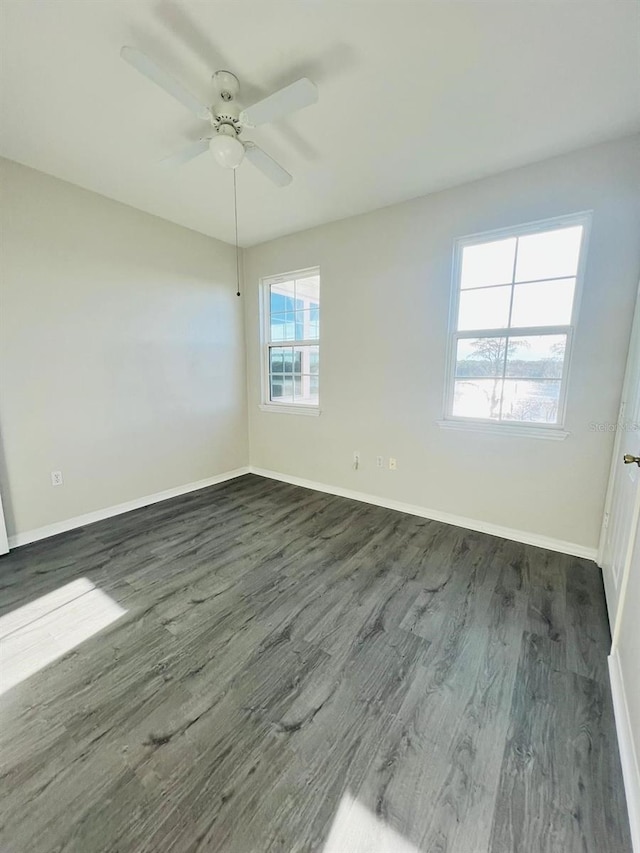 unfurnished room featuring dark wood-style floors, a ceiling fan, and baseboards