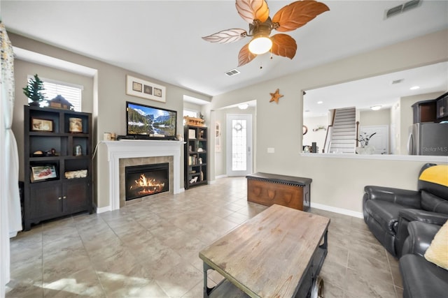 living area featuring baseboards, visible vents, a ceiling fan, and a tile fireplace