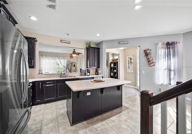 kitchen with a kitchen island, freestanding refrigerator, light countertops, a kitchen bar, and a sink