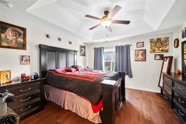 bedroom with dark wood-type flooring, a raised ceiling, baseboards, and a ceiling fan