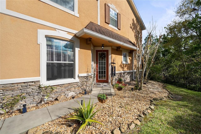 doorway to property featuring stone siding, fence, and stucco siding