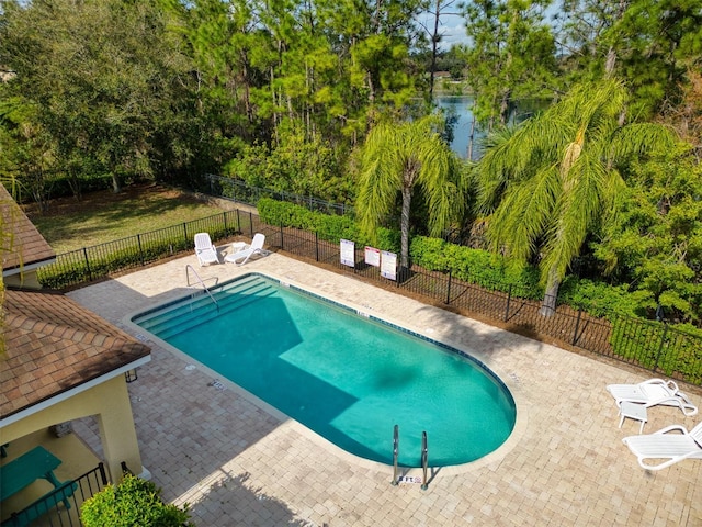 community pool featuring a patio, a water view, and fence