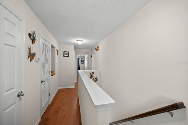 hallway featuring a textured ceiling, baseboards, wood finished floors, and an upstairs landing