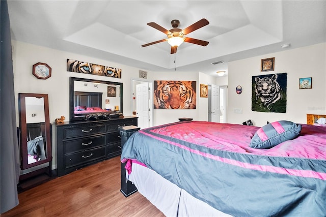 bedroom with visible vents, a tray ceiling, ceiling fan, and wood finished floors