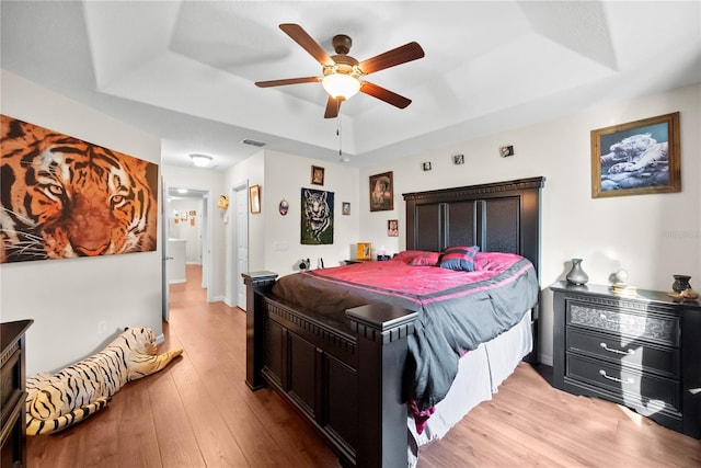 bedroom with ceiling fan, a tray ceiling, light wood-type flooring, and visible vents