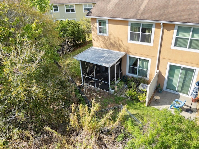 rear view of property featuring roof with shingles, stucco siding, a sunroom, a patio area, and fence