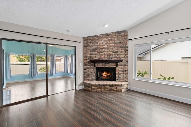 unfurnished living room featuring baseboards, wood finished floors, vaulted ceiling, a textured ceiling, and a brick fireplace