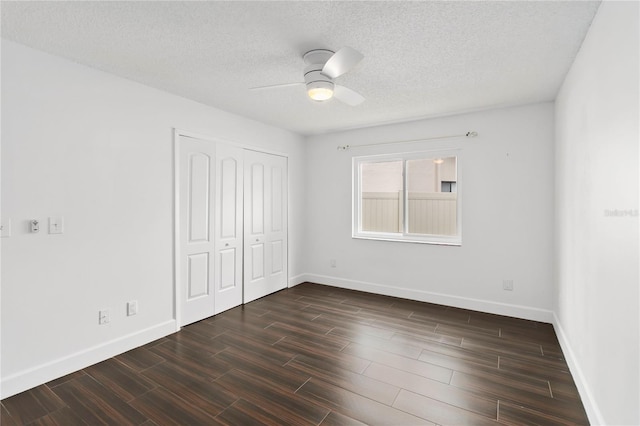 unfurnished bedroom featuring a textured ceiling, baseboards, dark wood finished floors, and a closet