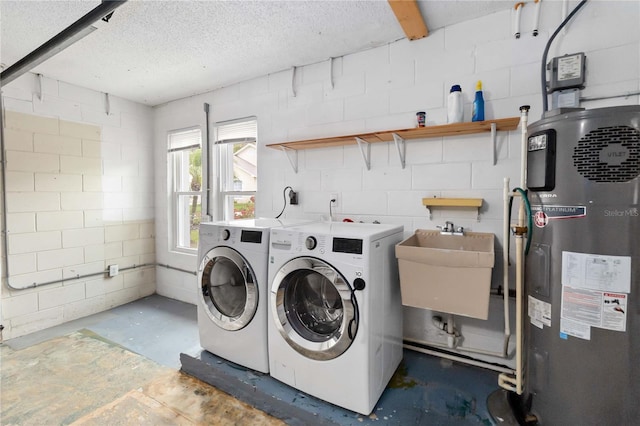 laundry area with concrete block wall, a textured ceiling, washing machine and dryer, water heater, and a sink