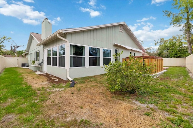 back of house with a yard, a chimney, a fenced backyard, and central air condition unit