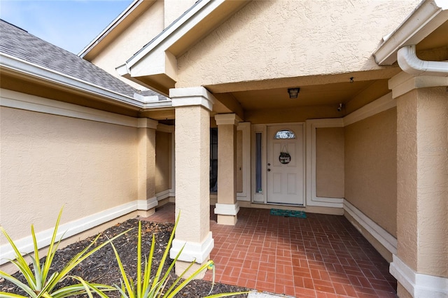 entrance to property featuring a shingled roof and stucco siding