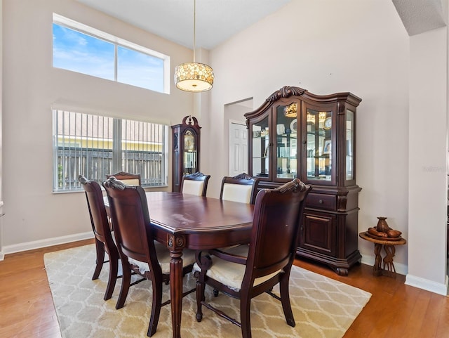 dining room with a towering ceiling, light wood-style flooring, and baseboards