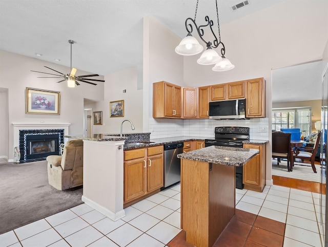 kitchen featuring appliances with stainless steel finishes, open floor plan, a sink, a tile fireplace, and a peninsula