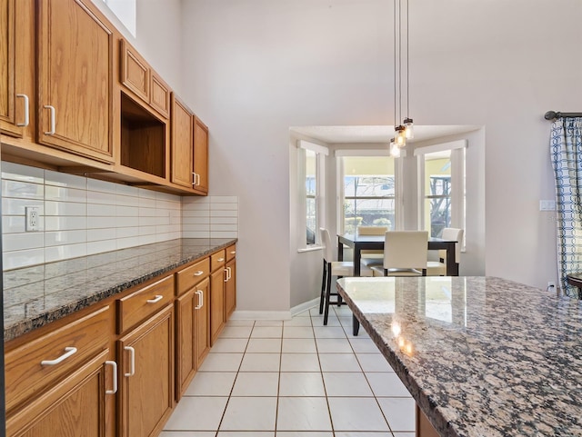 kitchen featuring light tile patterned floors, decorative backsplash, a towering ceiling, brown cabinets, and pendant lighting