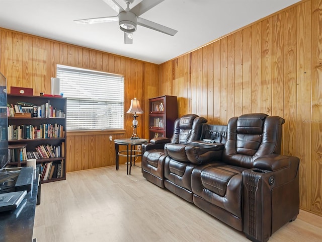 living area featuring ceiling fan, wooden walls, and wood finished floors