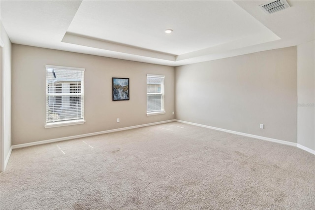 carpeted empty room with a raised ceiling, visible vents, and baseboards