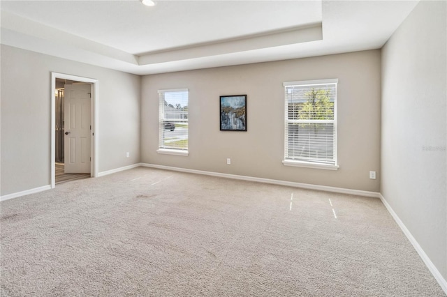 unfurnished room featuring light carpet, a raised ceiling, and baseboards