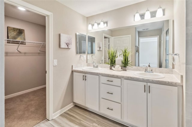 full bath featuring double vanity, baseboards, a walk in closet, and a sink