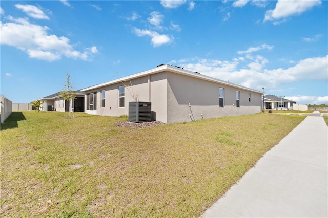 view of side of home featuring fence, a lawn, cooling unit, and stucco siding