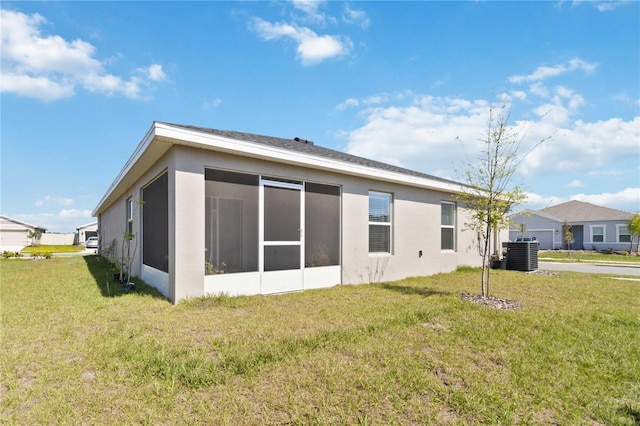 rear view of property featuring central air condition unit, a lawn, a sunroom, and stucco siding