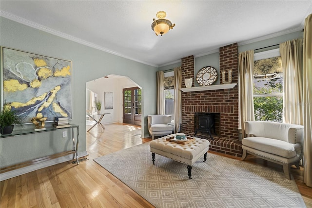 living room featuring arched walkways, wood finished floors, baseboards, a brick fireplace, and crown molding