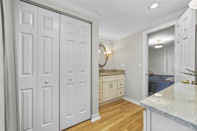 ensuite bathroom featuring wood finished floors, vanity, baseboards, a closet, and crown molding