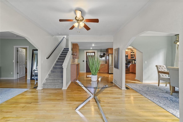 foyer entrance featuring light wood finished floors, baseboards, arched walkways, stairway, and ornamental molding