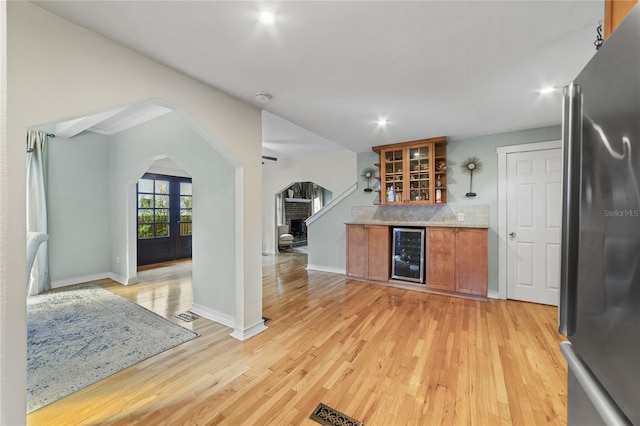 kitchen with arched walkways, wine cooler, light wood-type flooring, freestanding refrigerator, and brown cabinets