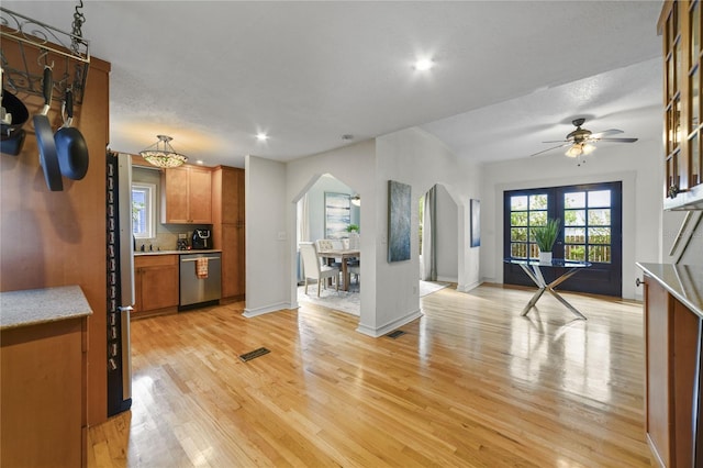 kitchen with arched walkways, brown cabinets, light countertops, light wood-type flooring, and stainless steel dishwasher