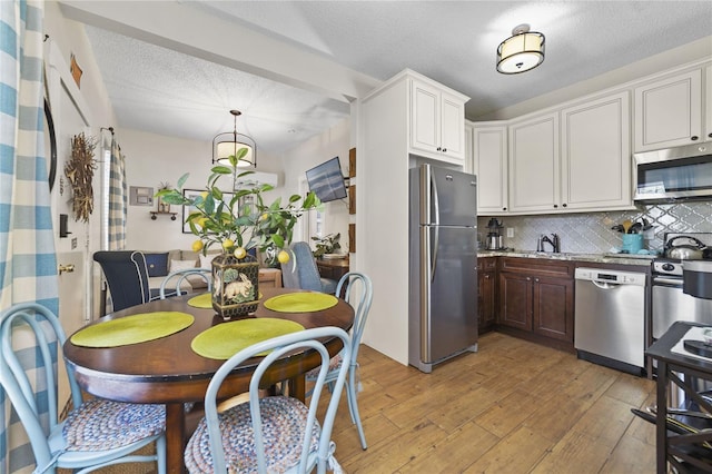 kitchen with a textured ceiling, a sink, appliances with stainless steel finishes, decorative backsplash, and light wood finished floors