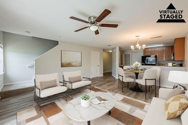 living room with light wood finished floors, visible vents, ceiling fan with notable chandelier, and baseboards