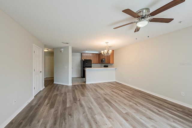 unfurnished living room with light wood-style flooring, ceiling fan with notable chandelier, and baseboards