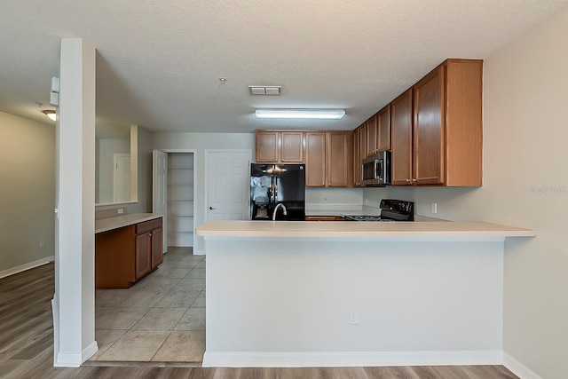 kitchen featuring visible vents, black appliances, a sink, a peninsula, and light countertops