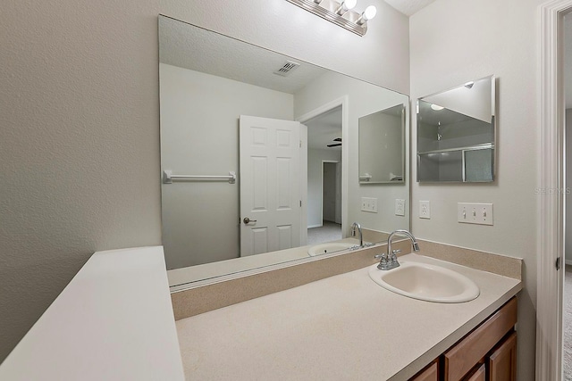 full bath with visible vents, vanity, and a textured wall