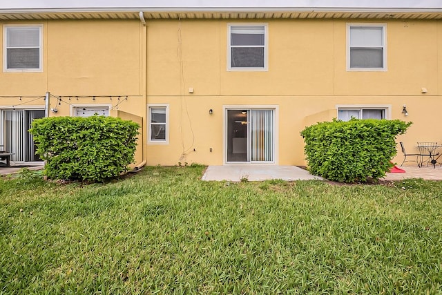 back of property featuring a patio area, a lawn, and stucco siding