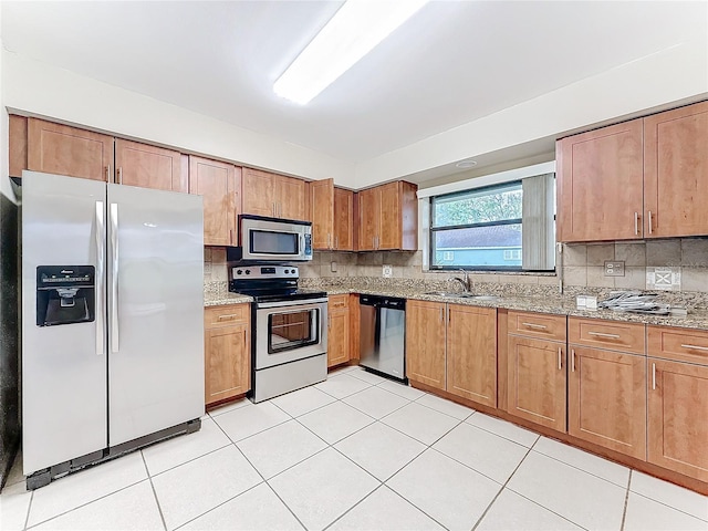 kitchen with stainless steel appliances, a sink, light stone counters, and tasteful backsplash