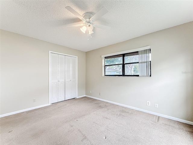 unfurnished bedroom featuring carpet floors, a closet, a ceiling fan, a textured ceiling, and baseboards